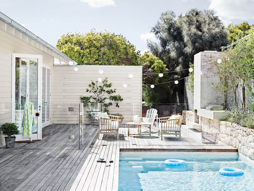 Neutral Exterior Backyard Wooden Deck with Pool and Plants and Brick Retainer Wall and Fairy Lights